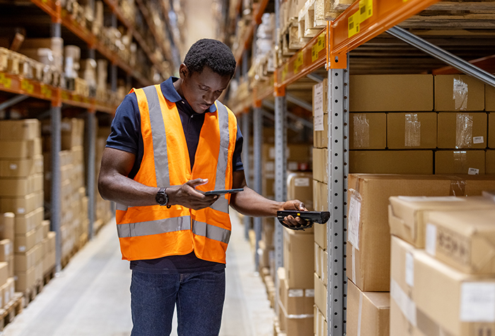 Young Man Scanning Boxes On The Rack With A Portable Scanner At Warehouse